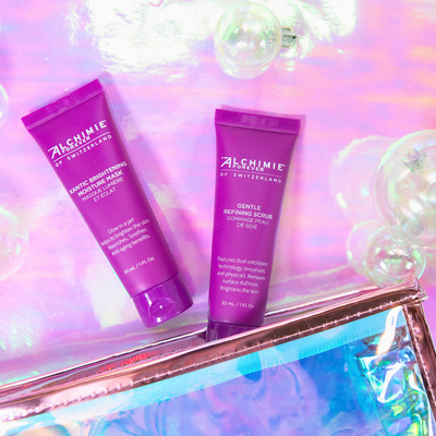 Two purple skincare products from Alchimie for Switzerland on a reflective surface with a colorful background.