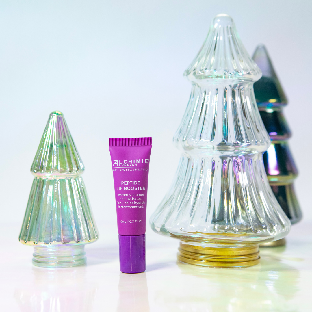 Purple Alchimie Forever Peptide Lip Booster tube between two glass Christmas tree-shaped containers on a white background